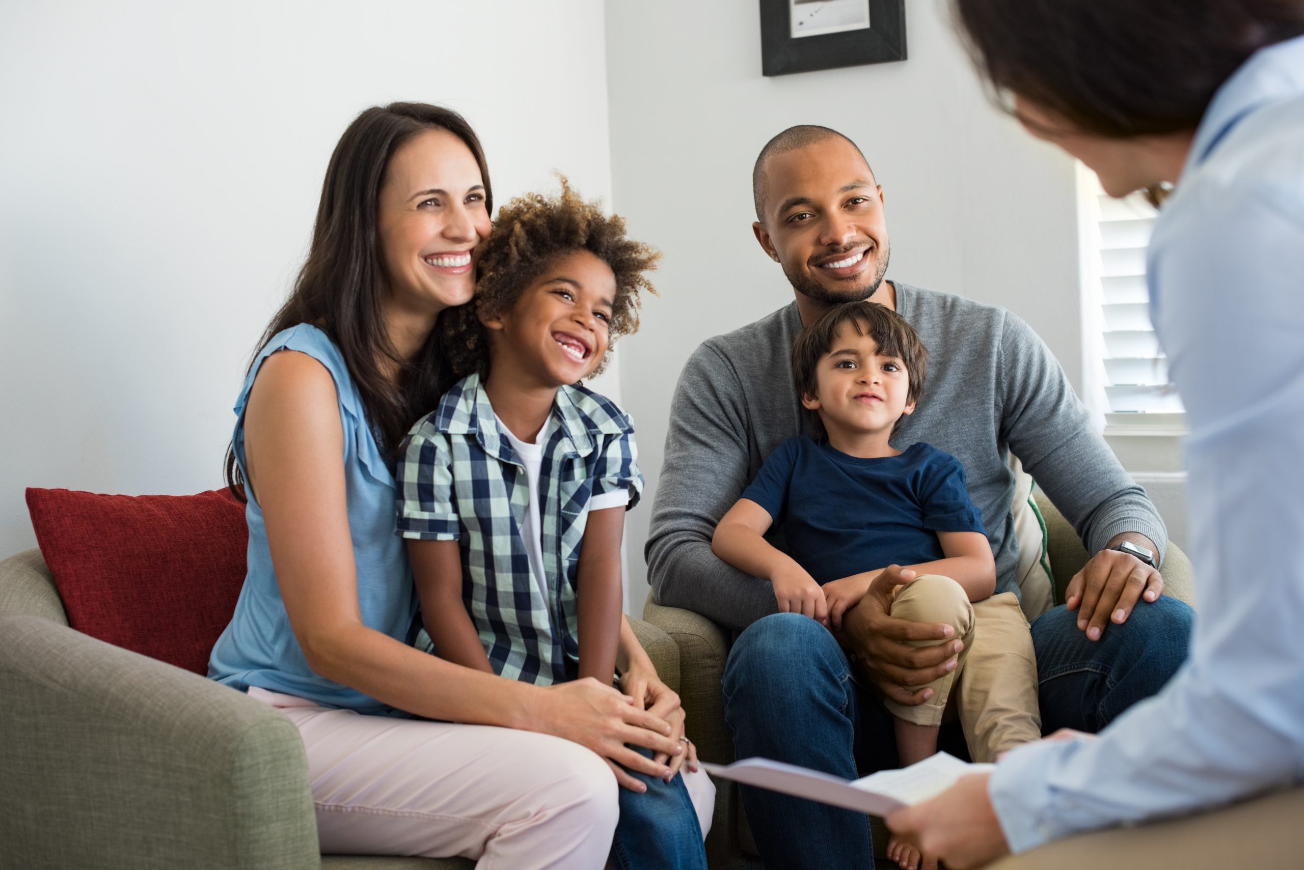 Happy young family sitting on the couch and talking with a family counselor. Smiling parents with adopted children discussing with a counselor. Multiethnic family meeting a financial agent.