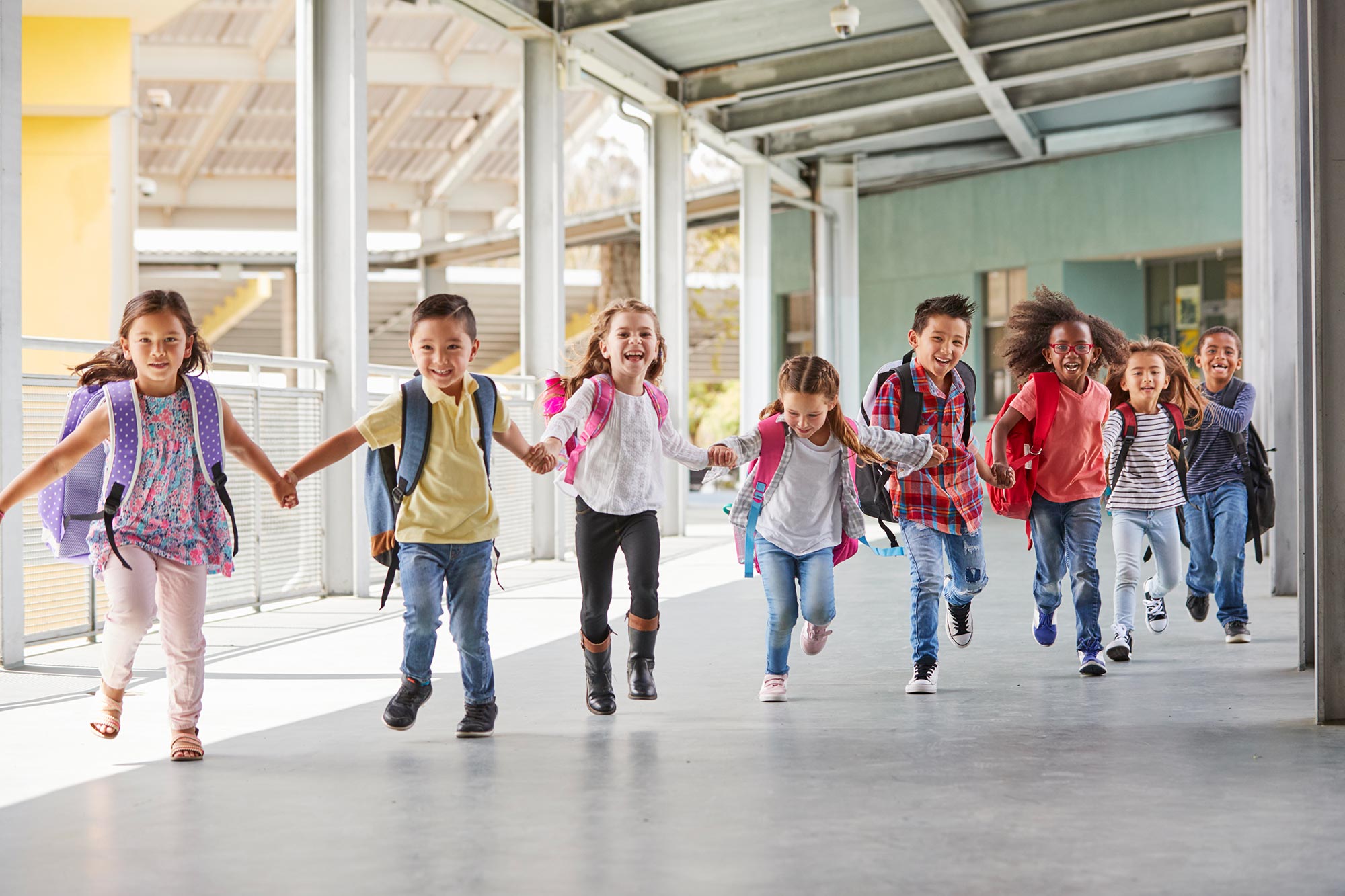 Young children holding hands and running through school halls