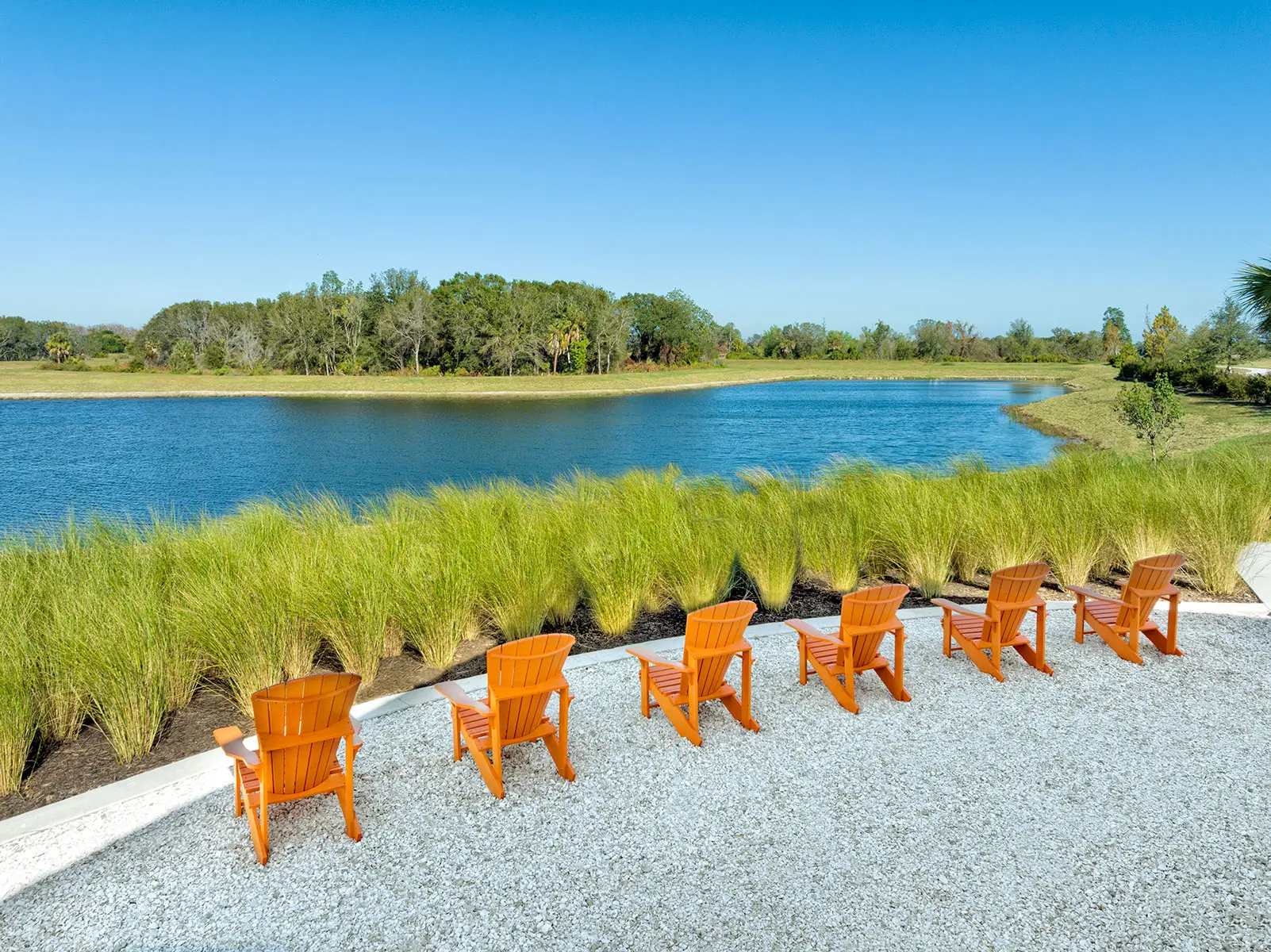 Orange outdoor chairs lining the grassy edge of a river at North River Ranch, Parrish, FL